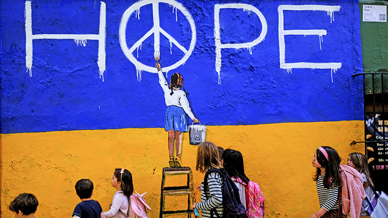 Ein Wandgemälde zeigt ein Mädchen, das das Wort "Hope" mit integriertem Peace-Zeichen malt